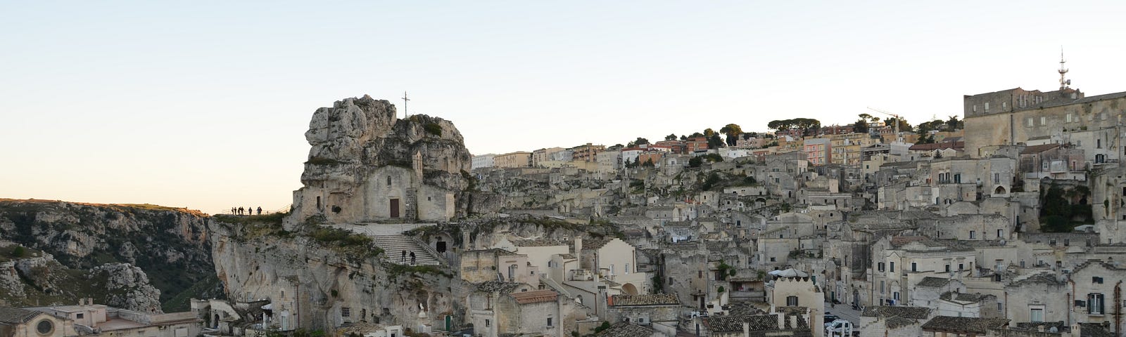 A hillside is covered with stone buildings of various heights especially on the left side of the photo — many have arched windows. On the right side, there is a courtyard in front of a building.
