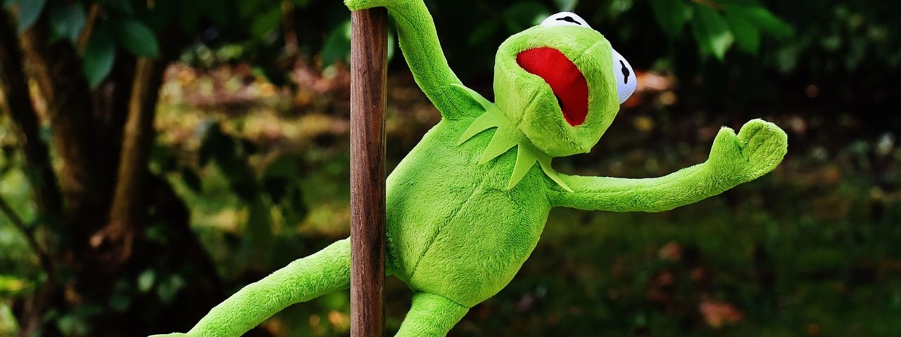Kermit the frog on a pole. He is doing a pole dance move.