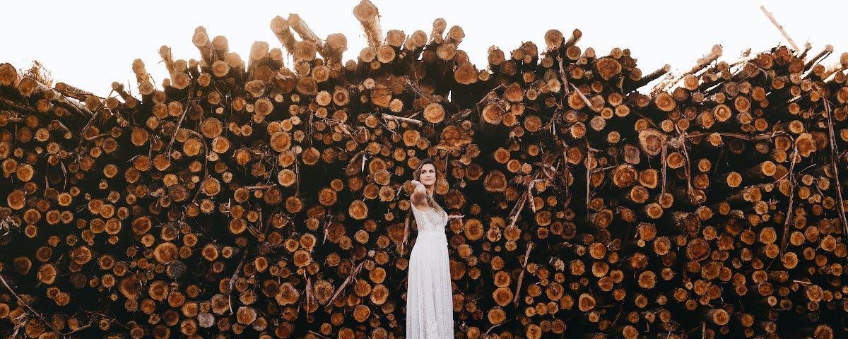 A woman in a long, white dress, apparently floating in mid-air in front of a huge pile of logs.