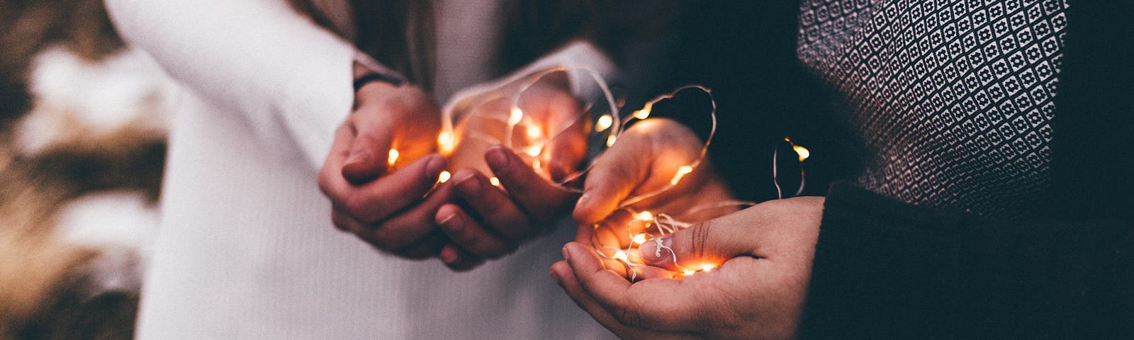 Close-up photo of two person holding lighted string lights.