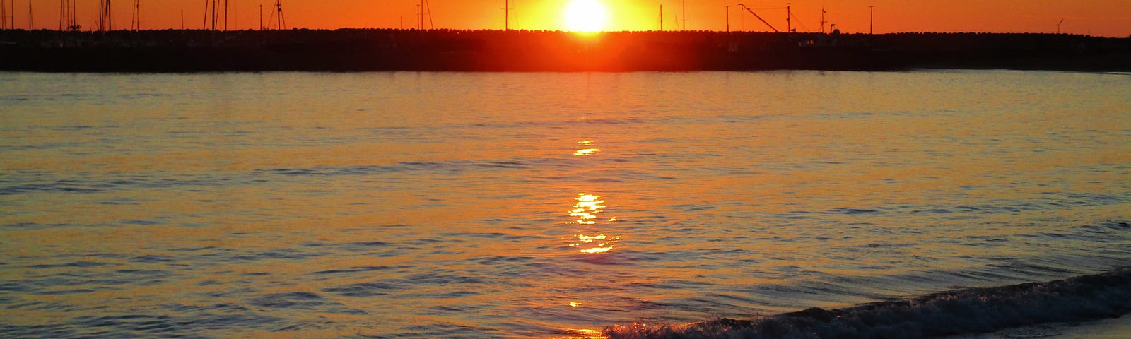 A beach scene at sunrise with a line of sunlight reflected in the water.