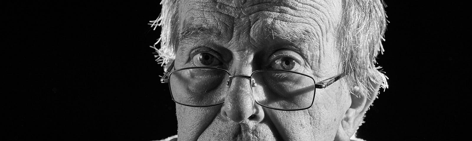 Black and white photo of an old man with glasses, looking morose