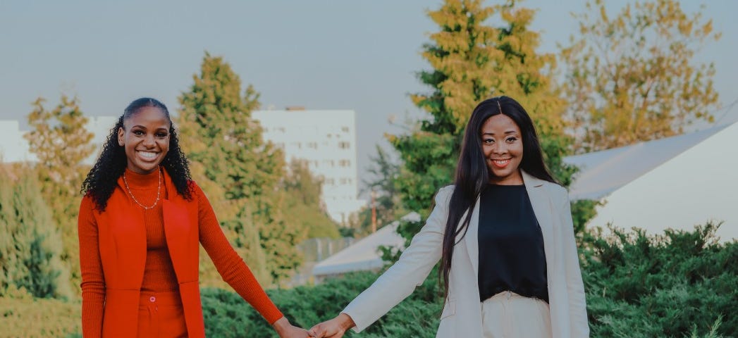 A beautiful Black lesbian couple hold hands while smiling.