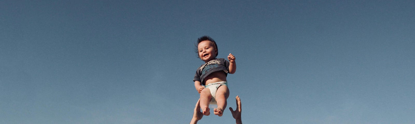 Blue sky back ground. Happy baby in mid-air as a man throws him up to catch him again.