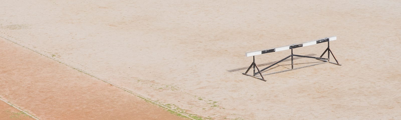 A black and white hurdle sits beside an athletic track.