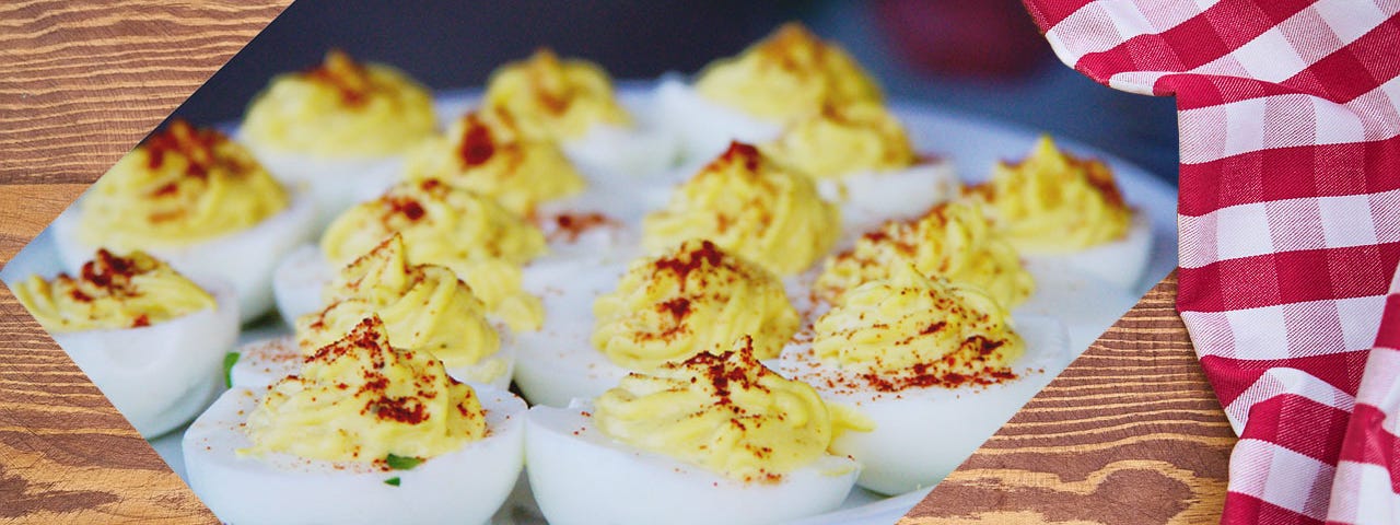 Deviled eggs on a white plate, against a background of a wooden table with a white and red checked tablecloth