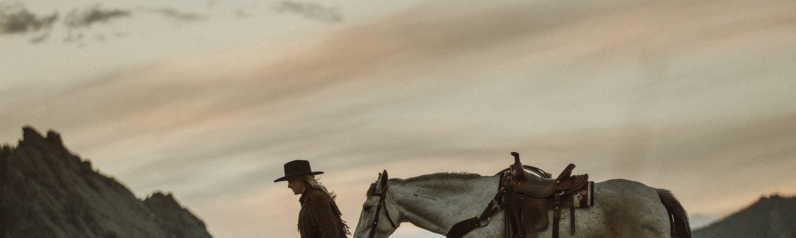 Woman leading horse through rustic mountains at sunset.