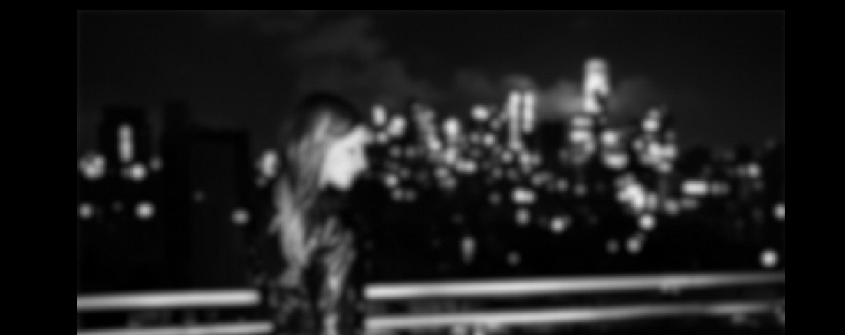 A blurred image of a woman standing outside on a balcony at nighttime