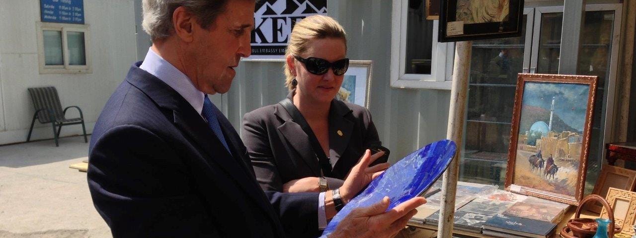 Jennifer Davis and former Sec. of State John Kerry inspect a piece of pottery at an outdoor market