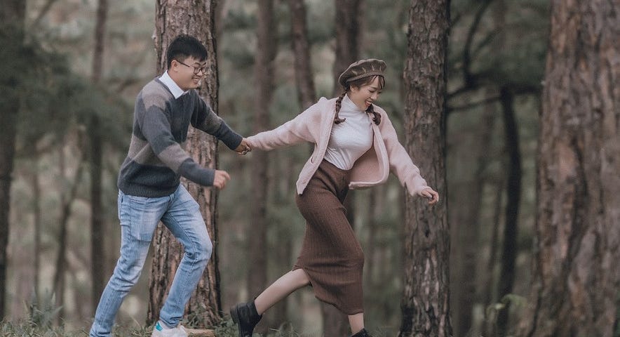 Photo of a couple running in the woods while holding hands