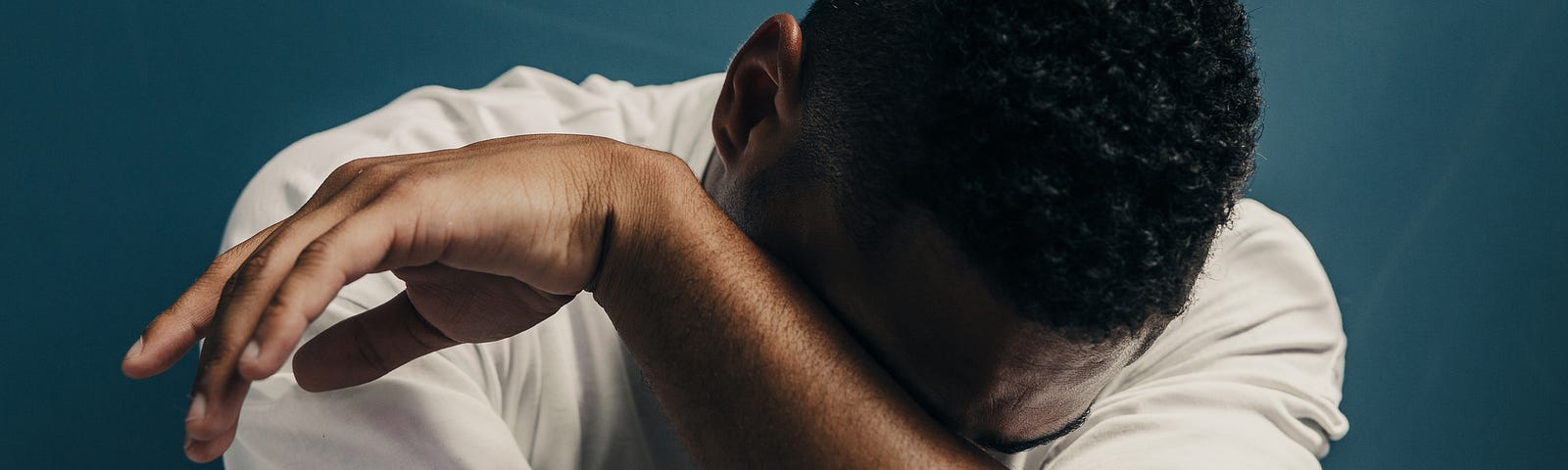 A Black man hides his face in his arm and apprears to be crying.