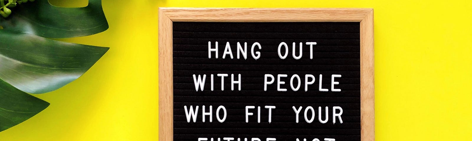 A sign reading, “Hang out with people who fit your future not your history,” stands against a yellow background.