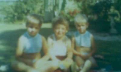 A blurry blue-green vintage family photo of three children posing for the camera, smiling in summer clothes.