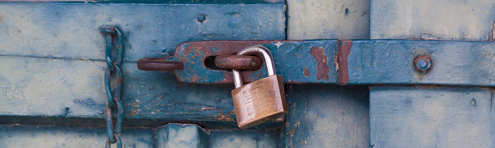 A padlock securing a rustic blue door.