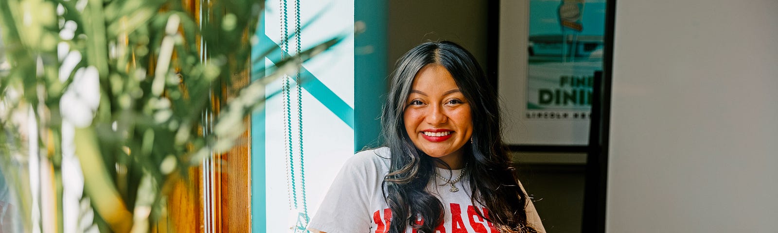 Isela smiles for a photo in the library with the sun streaming in through the windows