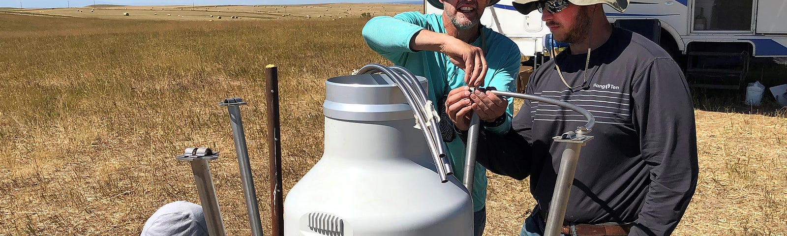 Three men install equipment on the Montana prairie near a camper.