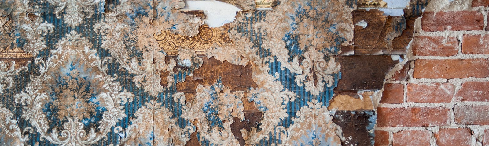 Image of old wallpaper, peeling paint and exposed brickwork