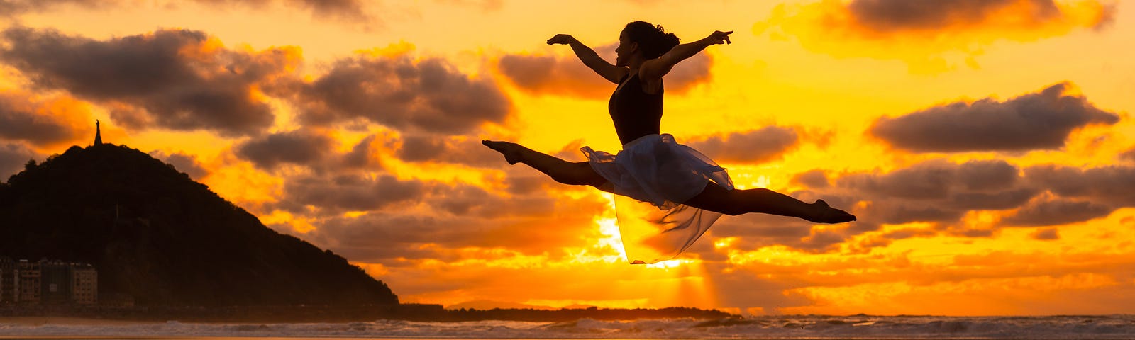 Young dancer on the beach at sunset performing a jump with the sea in the background