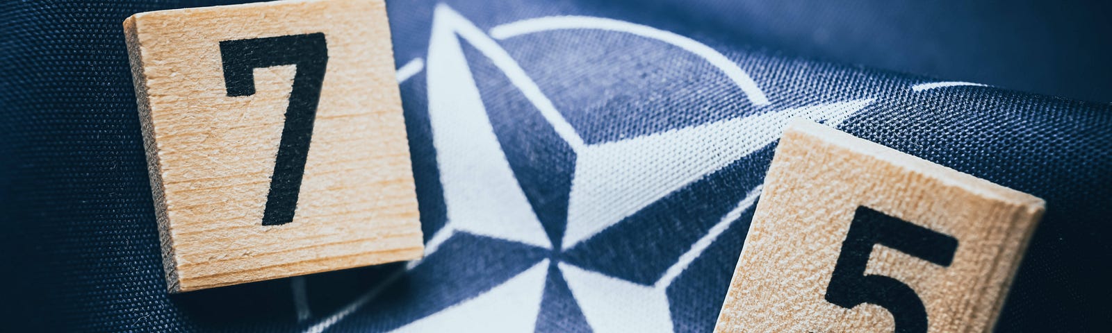 Wood blocks with the numbers 7 and 5 on top of fabric showing the NATO emblem. Photo by Christian Ohde/IMAGO/Reuters