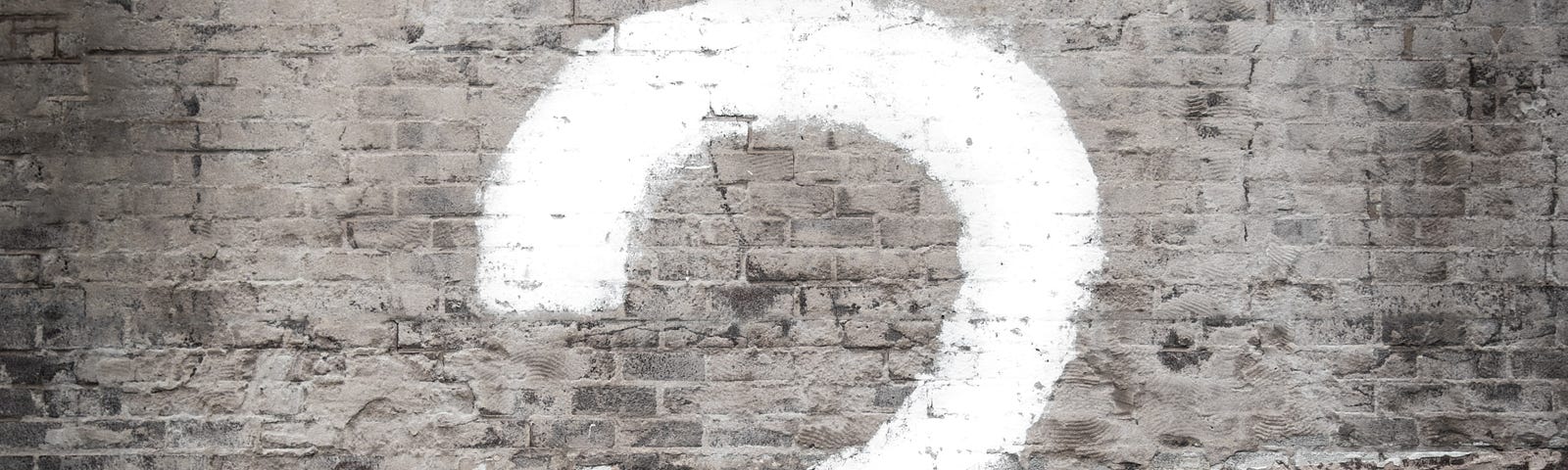 A large white question mark sprayed on a faded brick wall