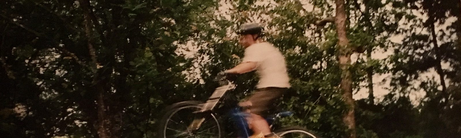 A blurry photo of a boy on a bicycle going over a jump. The bike and the boy are in the air