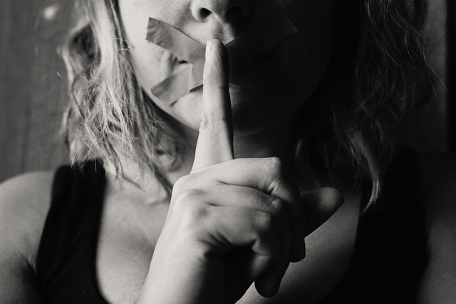 Woman with index finger over mouth as if to say “be quiet”