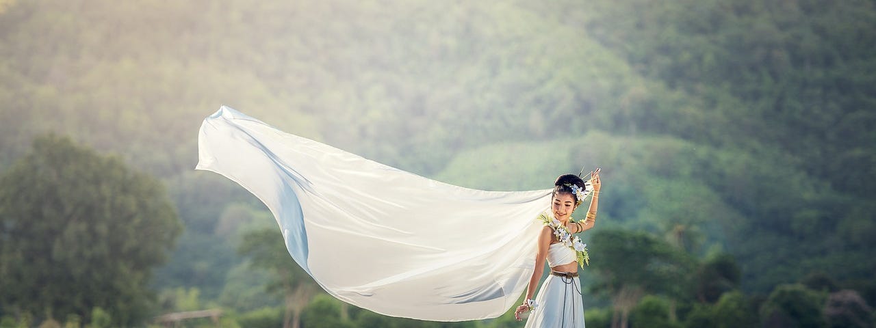 A young girl standing in a field with the wind blowing her veil.