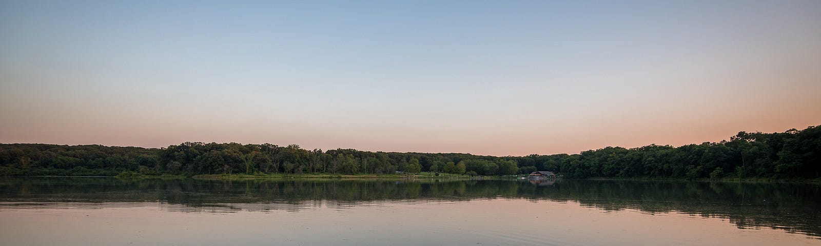 A large lake with a tree lined shore at sunset.