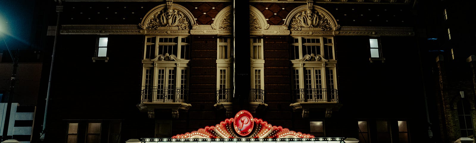 The front of the Paramount Theatre House (Austin, TX), with a marquis lit up in red, white, and black. The letters on the marquis read: “In order for us to be all together, for now we must remain apart.”