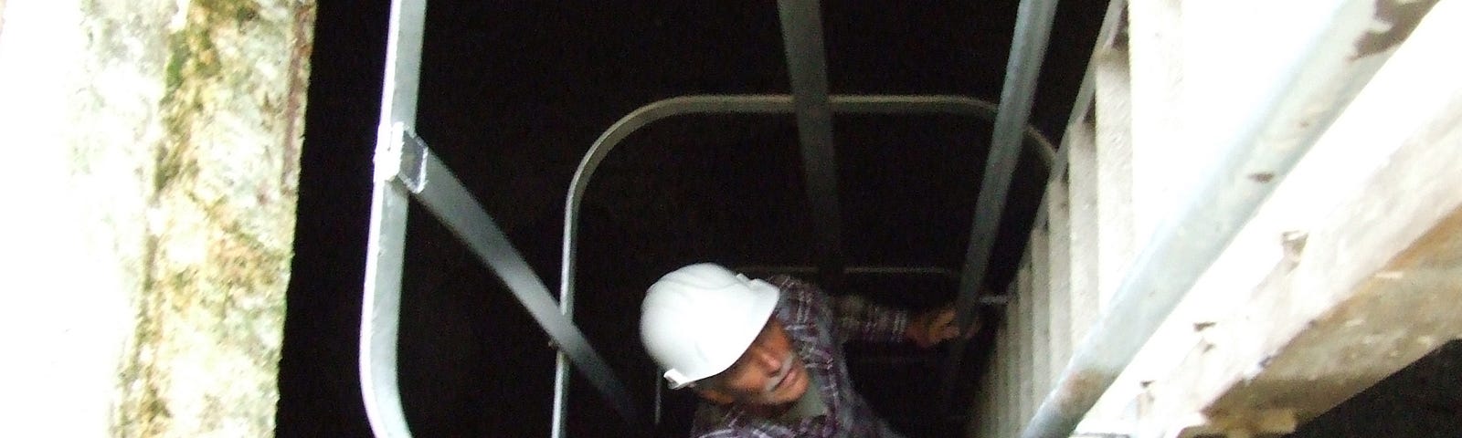 Man in white hard hat going down a safety ladder into Grime’s Graves