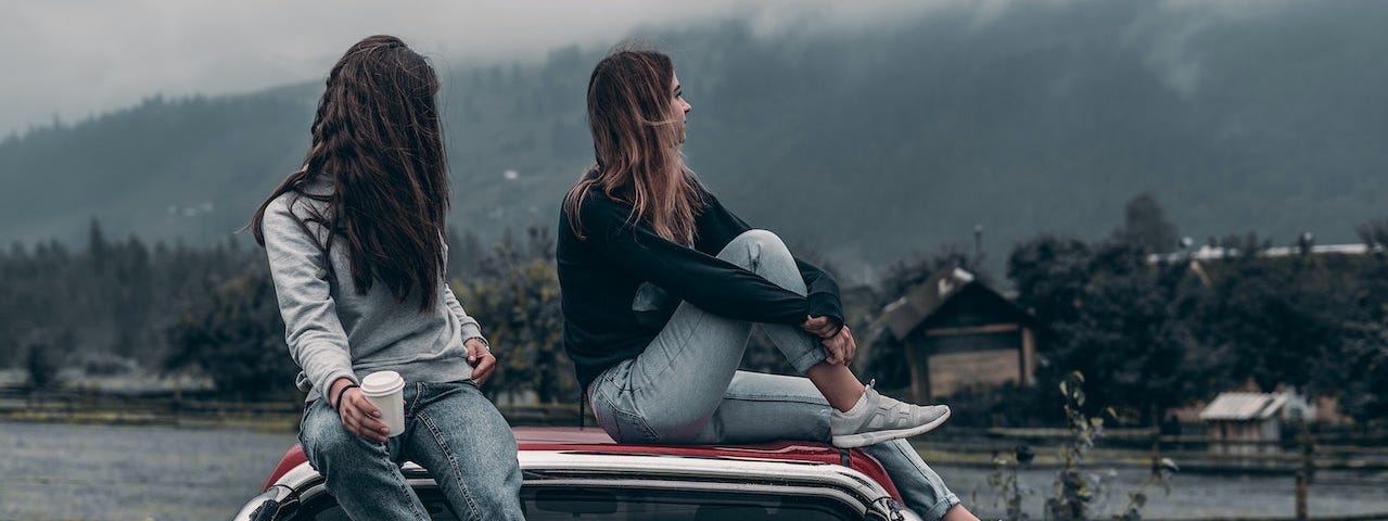 Two girls sitting on top of a car.