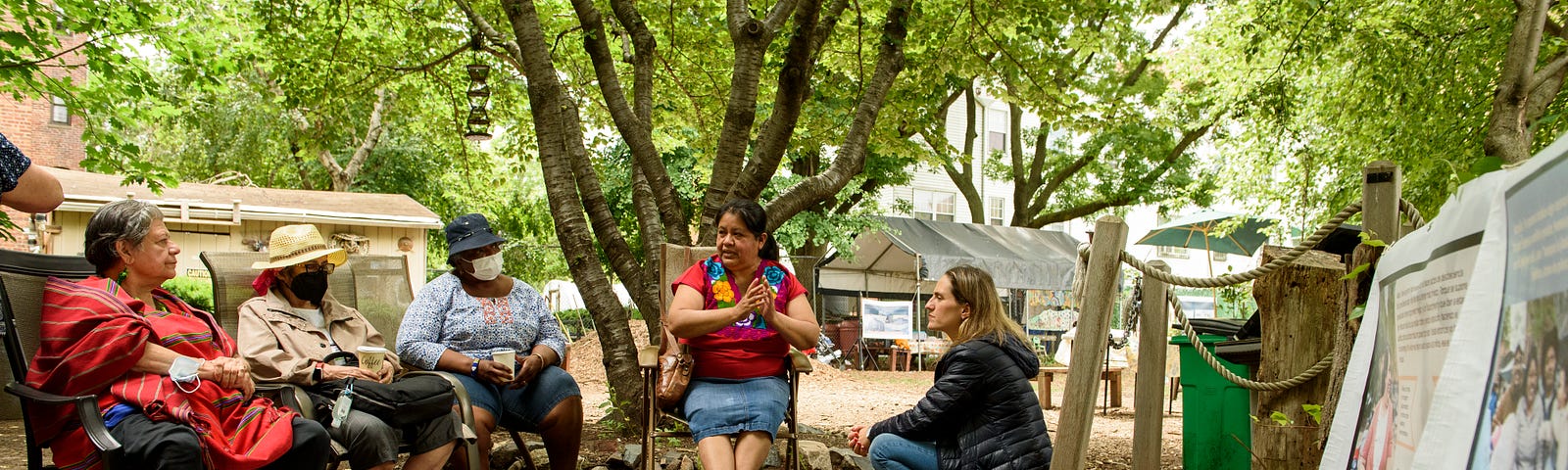 A group seated in the park, in conversation next to project banners