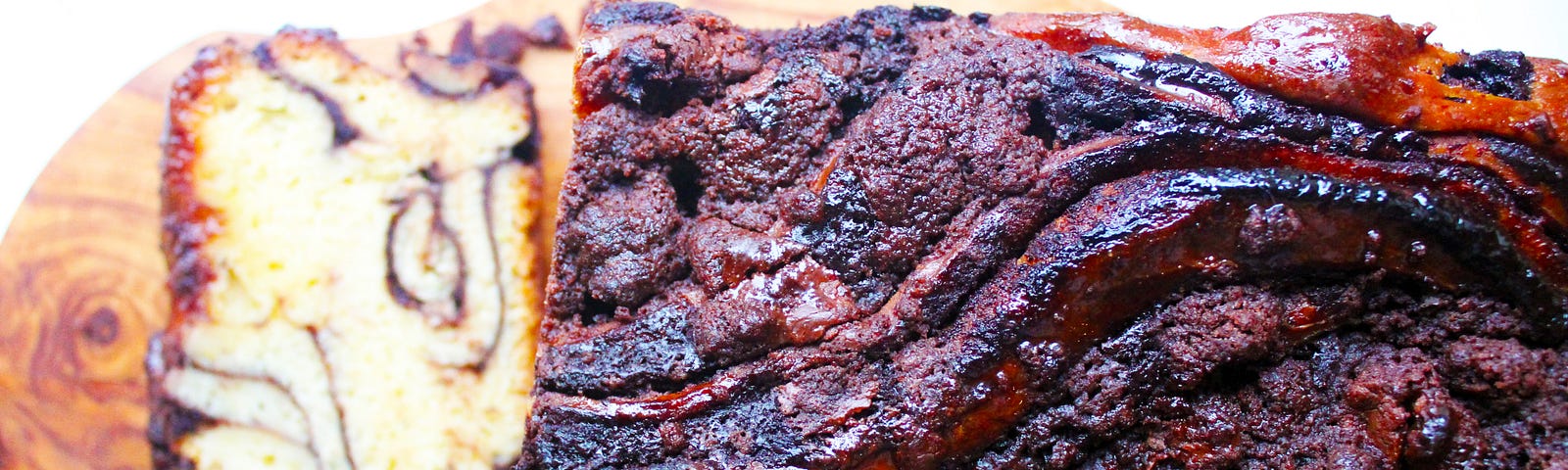 Chocolate babka loaf viewed from above on a wooden chopping board. A slice shows the inside chocolate swirls of the cake.