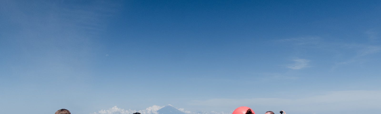 Four SCUBA divers floating at the ocean surface, within arms’ length of each other. Two divers float next to the dive site marker, a large red float ball.