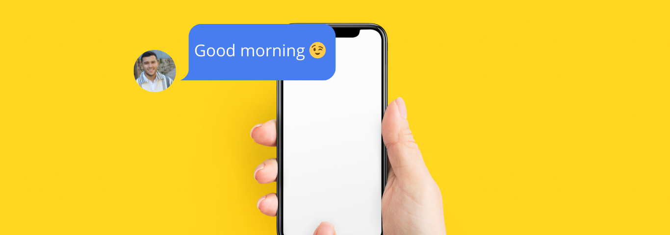 A hand holding a smartphone with a single message on the screen from Alex saying ‘Good morning’ accompanied by a winking emoji, on a bright yellow background. The rest of the screen is empty, indicating a waiting for a reply.