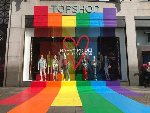 The shop window of Topshop on Oxford Street with a pride flag design seeping out the window onto the building and pavement.