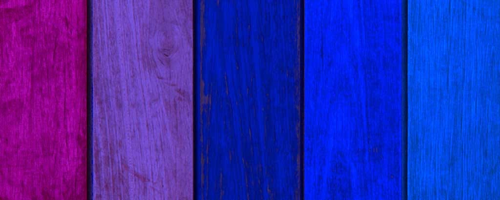Zoomed in picture of a wooden fence. Each of the boards is a different color, ranging from shades of purples to blues.