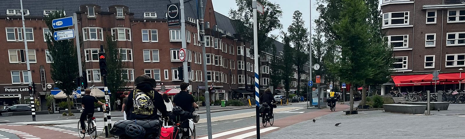 Four bikes ride through the streets of Amsterdam. One has a dog trailer attached.