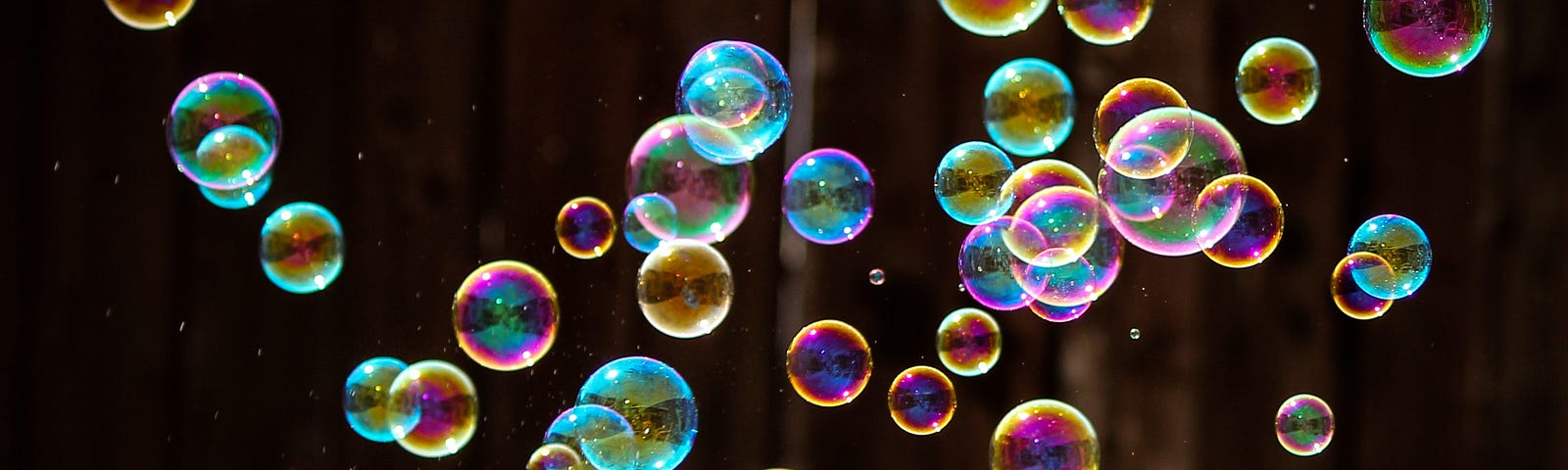 Many iridescent soap bubbles glimmering in darkness.