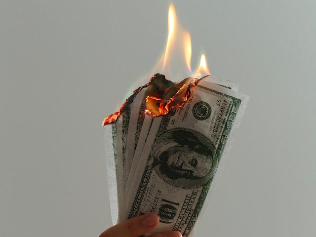 Hand holds US dollars on fire