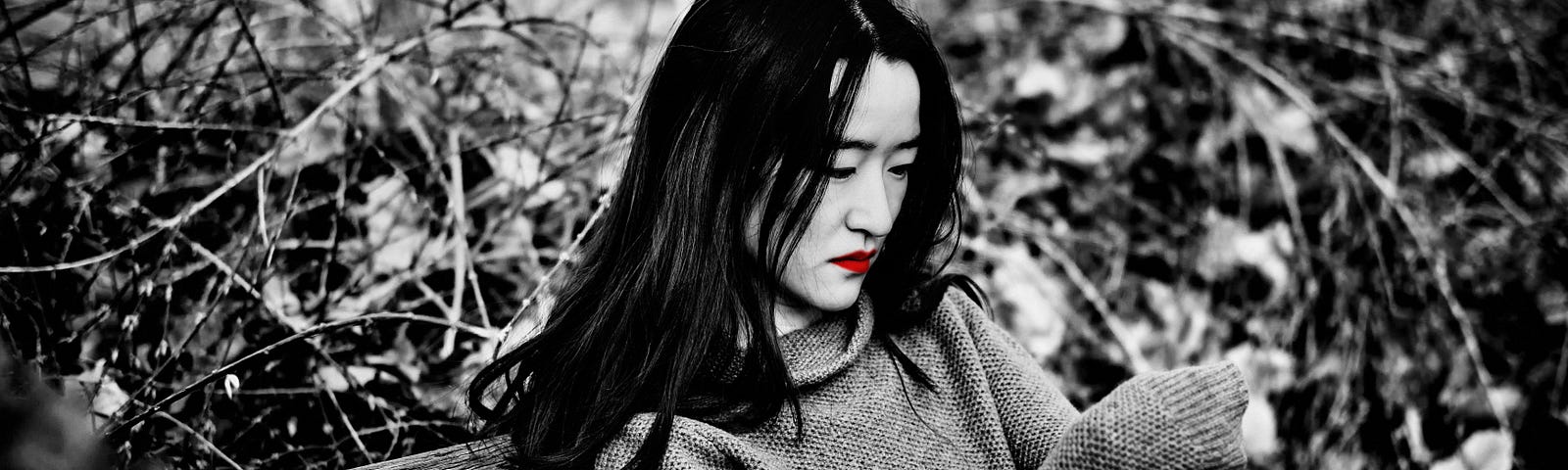 A black and white image of a sad Asian woman on a park bench. Her lips are red.