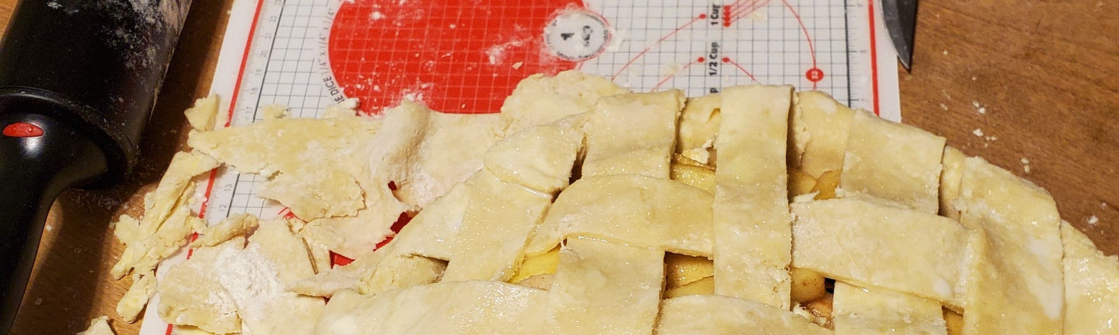 A rolling pin, flour, stick of butter, rolling mat, and unbaked pie sitting on a dining room table.