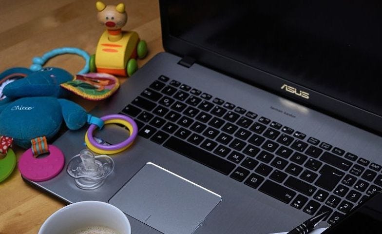 An openlaptop surrounded by children’s toys, with a cup of coffee in front of it and a pen, diary and phone resting on the left hand side