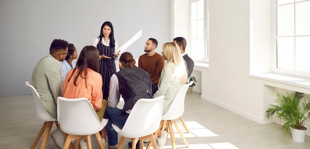 Diverse business team meeting in modern office. Group of people listening to serious young woman who’s standing in front of them, explaining some rules and talking about importance of management