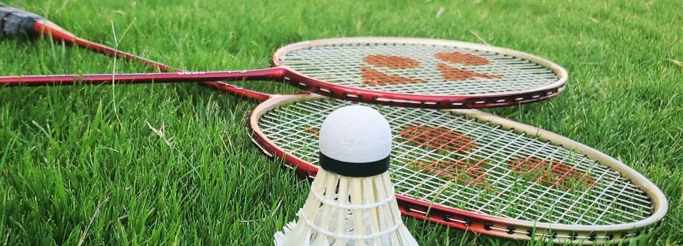 A shuttlecock and two badminton rackets are laid out on grass.