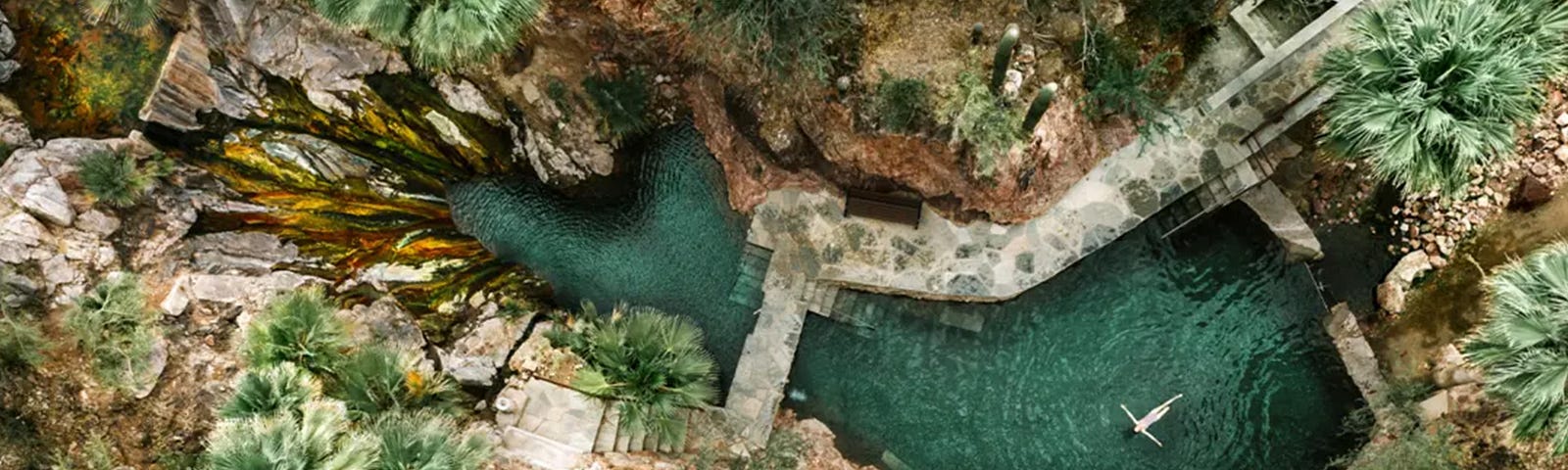 Resort guest floating in a natural hot springs pool, surrounded by desert landscape and flora.