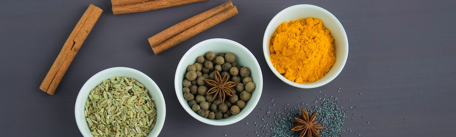 Three bowls of spices, including turmeric, along with cinnamin sticks