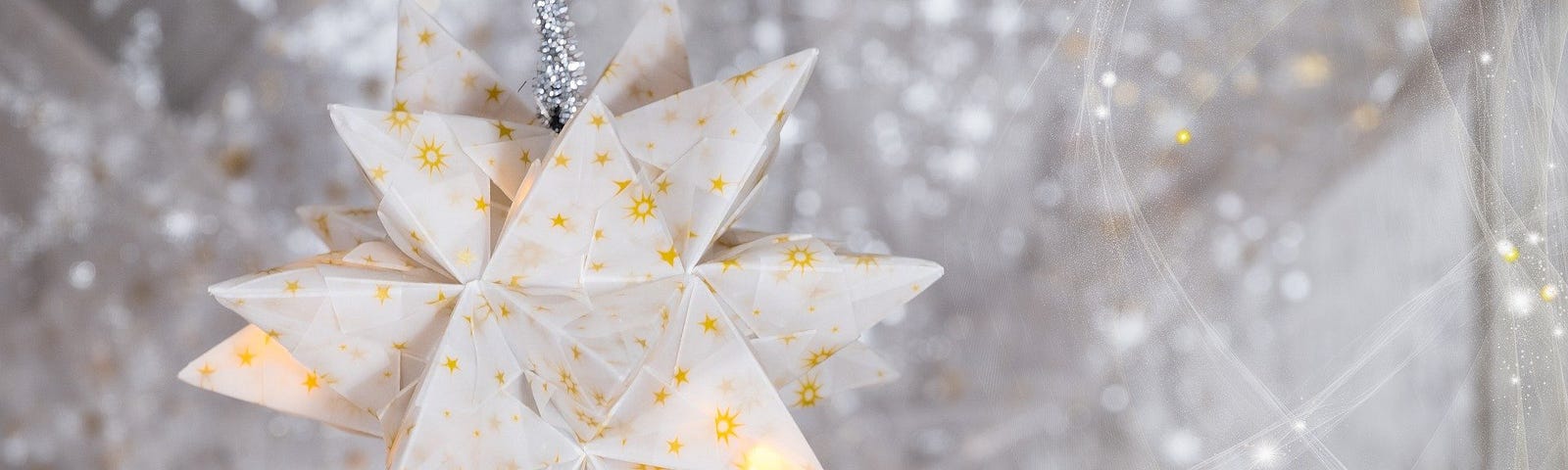 A gold and white paper star hanging in front of a background of silver stars