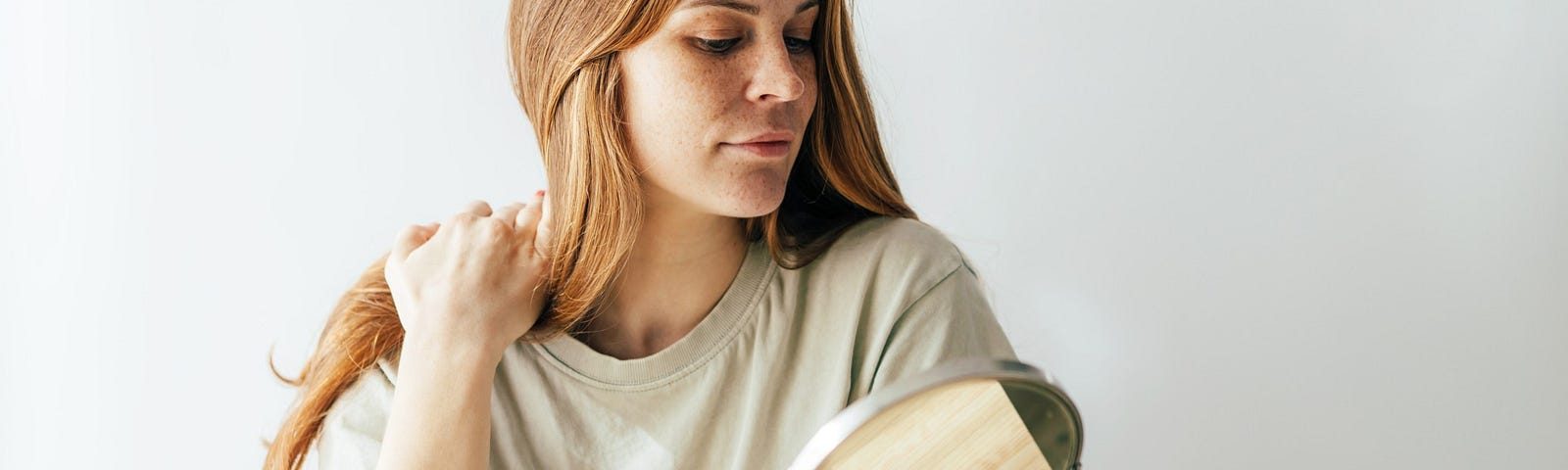 A woman plays with her hair while she stares into the mirror and smiles.