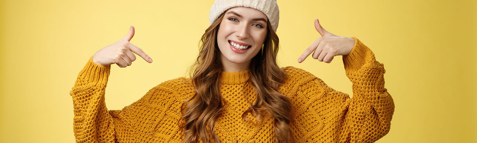Young woman in gold sweater and jeans pointing to herself as a winner.